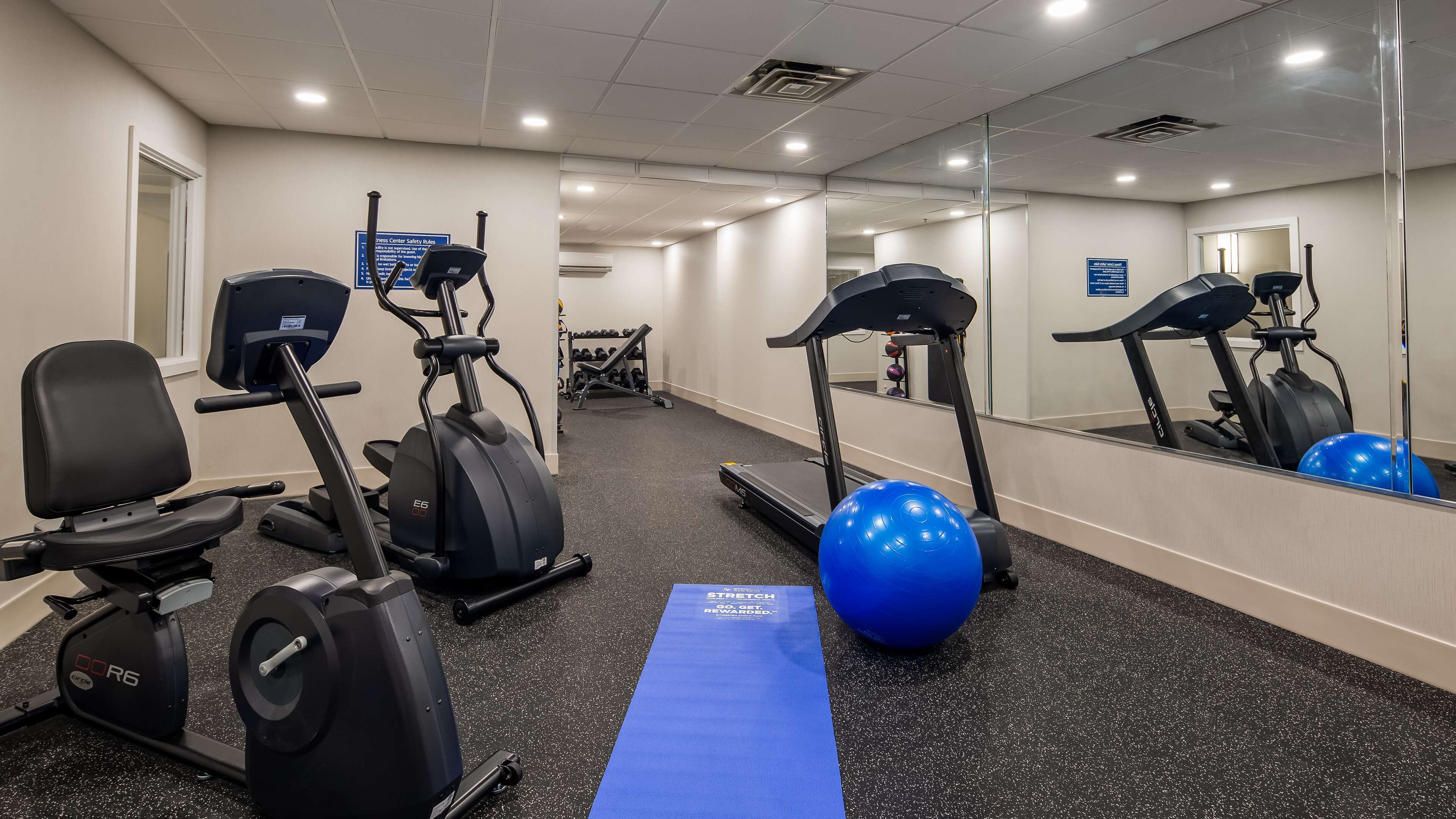 Une salle de sport équipée de machines de cardio, d’un ballon d’exercice bleu et d’un tapis d’étirement.