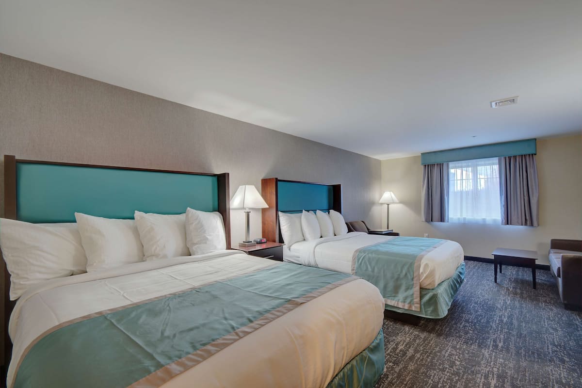 A hotel room with two beds, a desk, a chair, and a window with curtains.