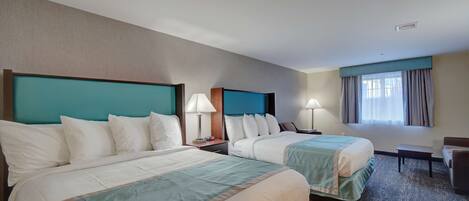 Habitación de hotel con dos camas, un escritorio, una silla y un ventanal con cortinas.