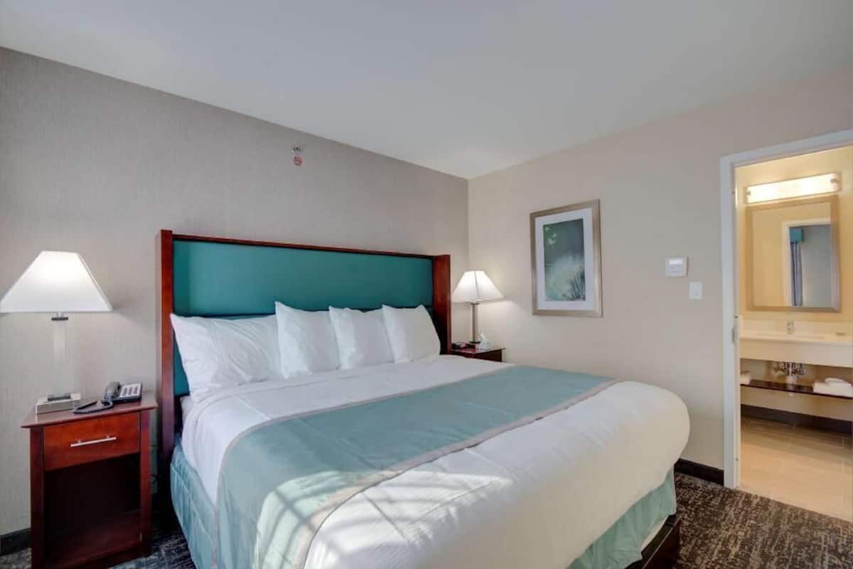 A hotel room with a bed, two bedside tables, a nightstand, a mirror, and a bathroom with a sink and mirror.