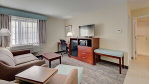 A hotel room with a sofa, a small table, a desk with a chair, a television, and a bench. - Best Western Hampshire Inn (Seabrook)