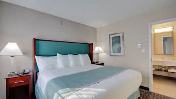 A hotel room with a large bed, two bedside tables, a nightstand, a bathroom with a sink and mirror, and a framed picture on the wall.