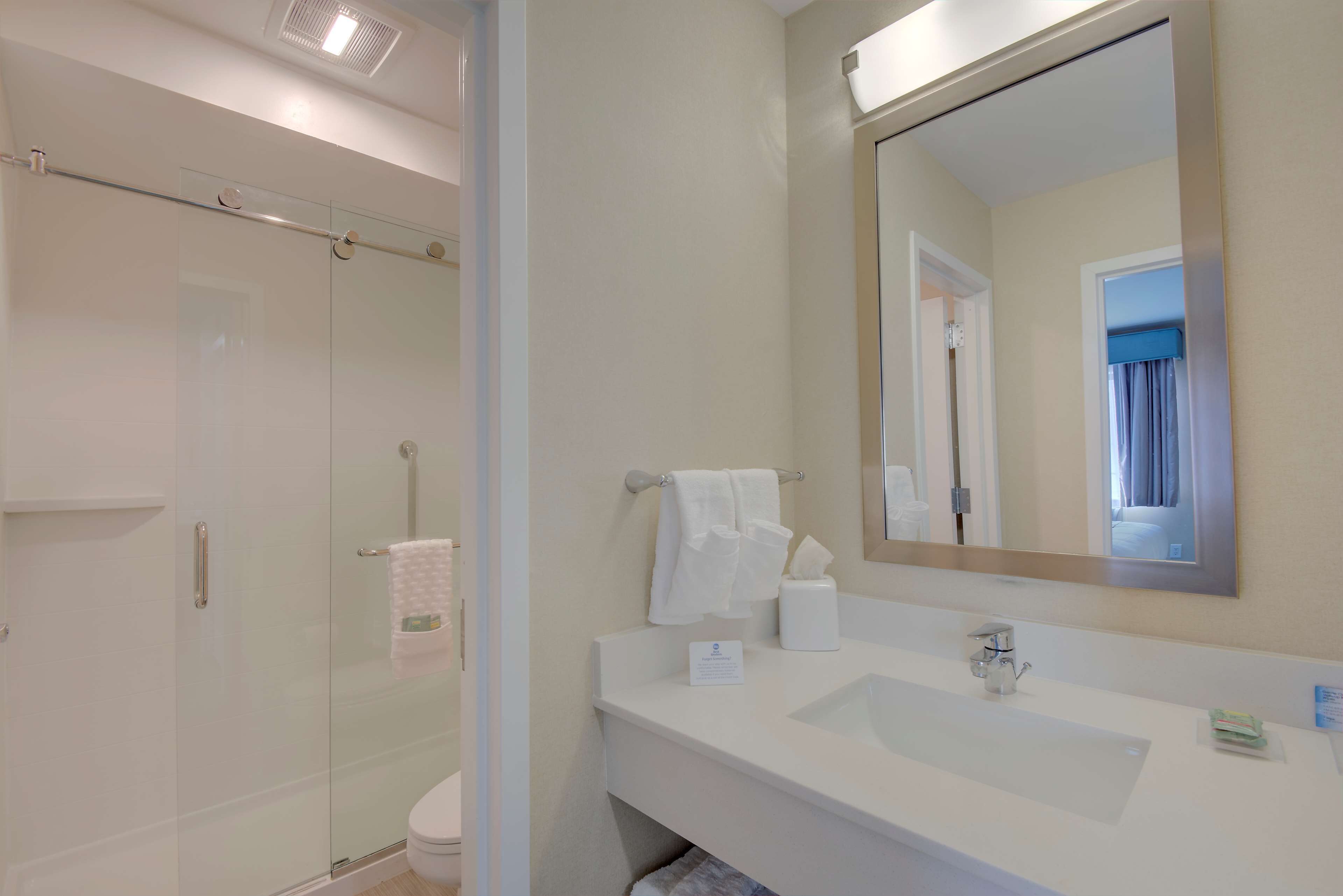 Une salle de bain moderne avec une douche à l’italienne en verre, un lavabo blanc et un grand miroir.