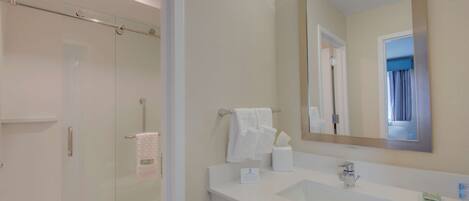 Une salle de bain moderne avec une douche à l’italienne en verre, un lavabo blanc et un grand miroir.
