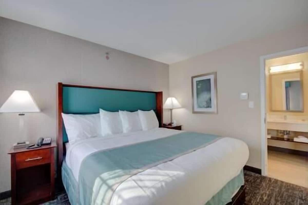 A hotel room with a bed, two bedside tables, a nightstand, a mirror, and a framed picture on the wall.