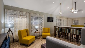 A modern living room with yellow armchairs, a dining area with a yellow bench, and a TV mounted on the wall. - Best Western Hampshire Inn (Seabrook)