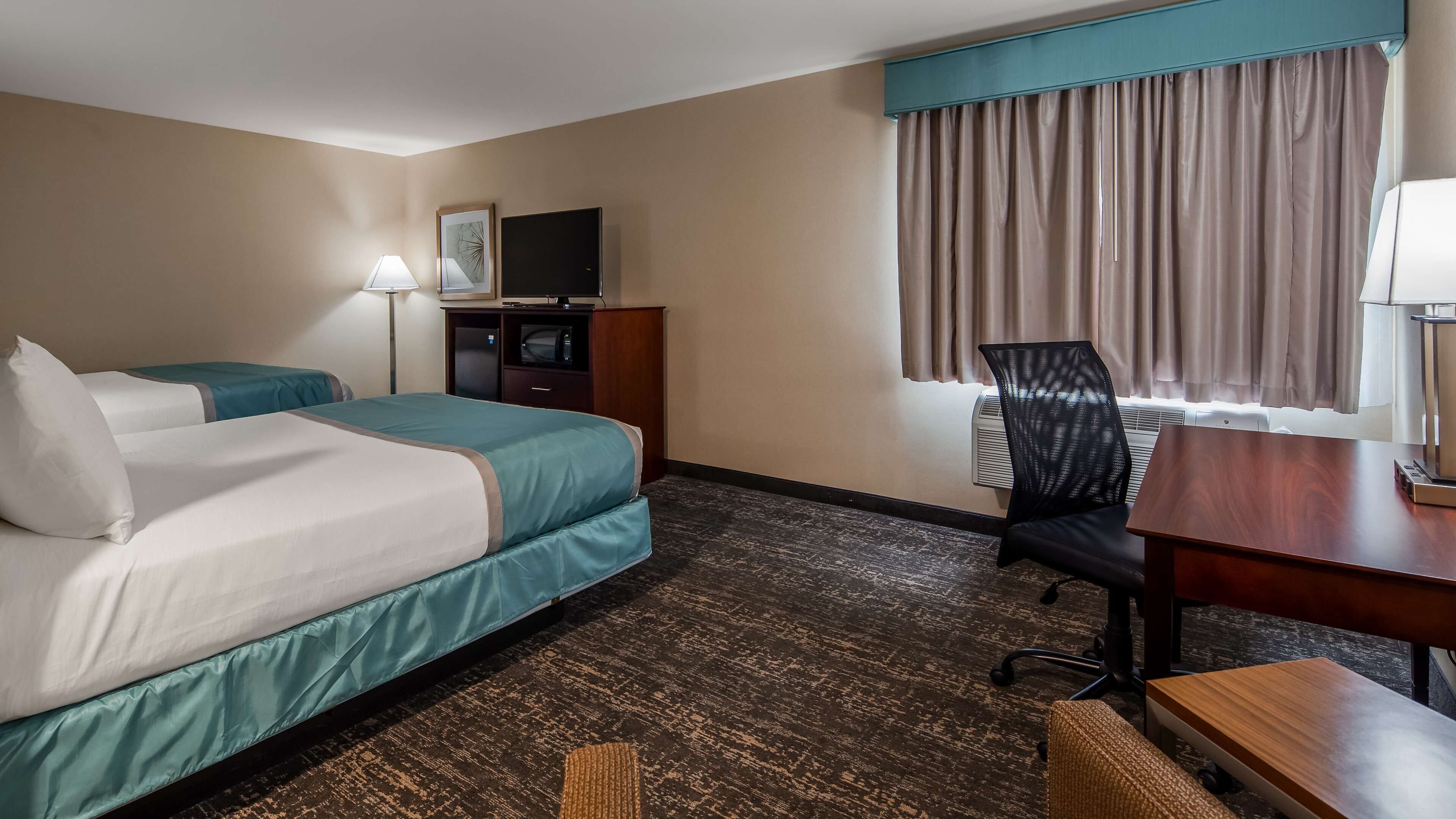 Une chambre d’hôtel avec deux lits, un bureau, une chaise, une télévision et une fenêtre avec des rideaux.