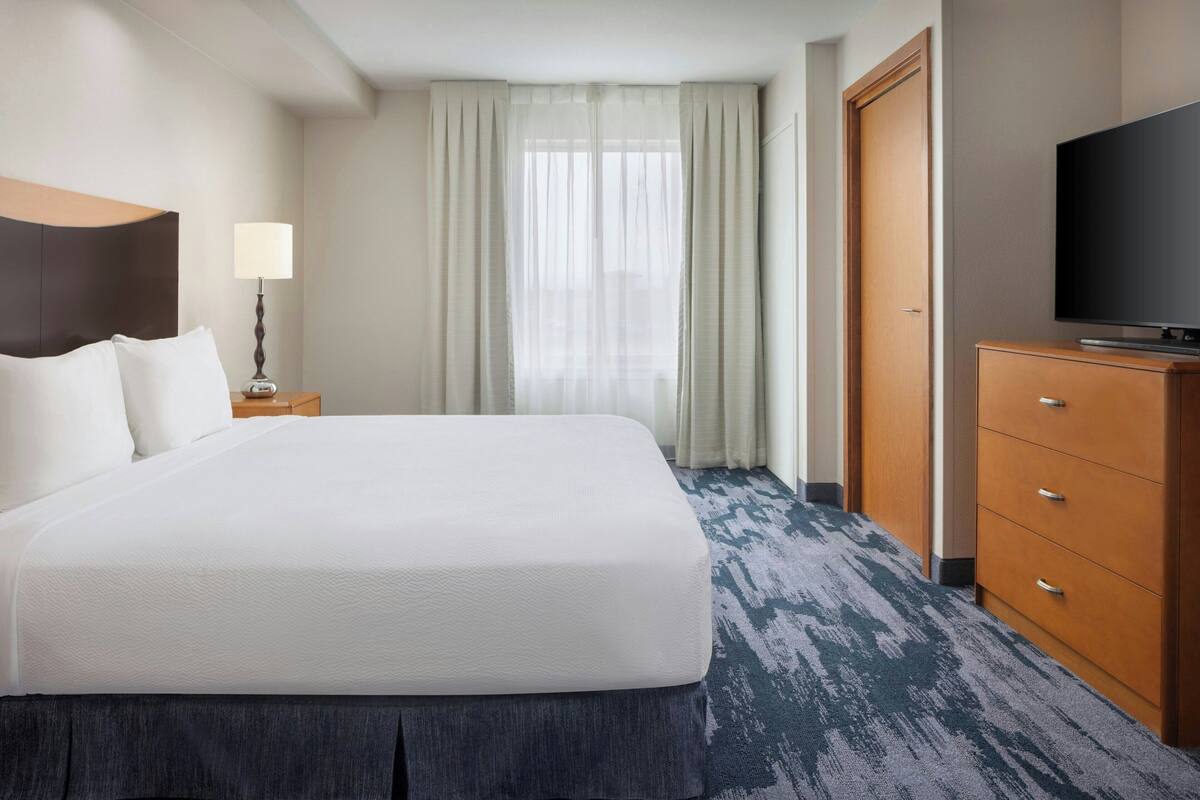 A hotel room with a large bed, a television, a wooden dresser, and a window with curtains.