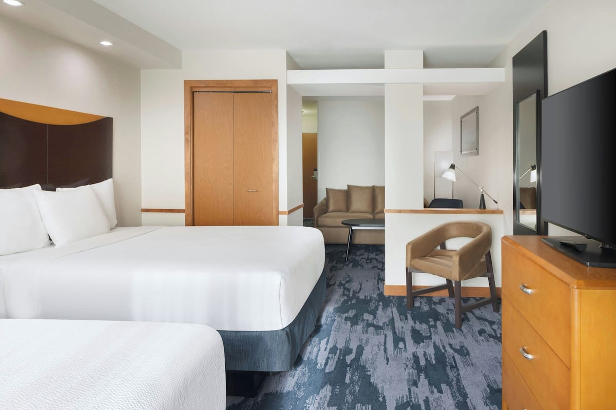A hotel room with a large bed, a desk, a chair, a television, and a wardrobe.