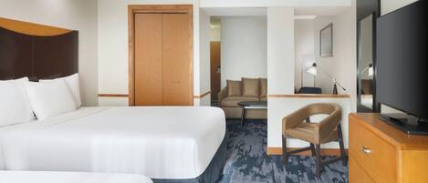 A hotel room with a large bed, a desk, a chair, a television, and a wardrobe.