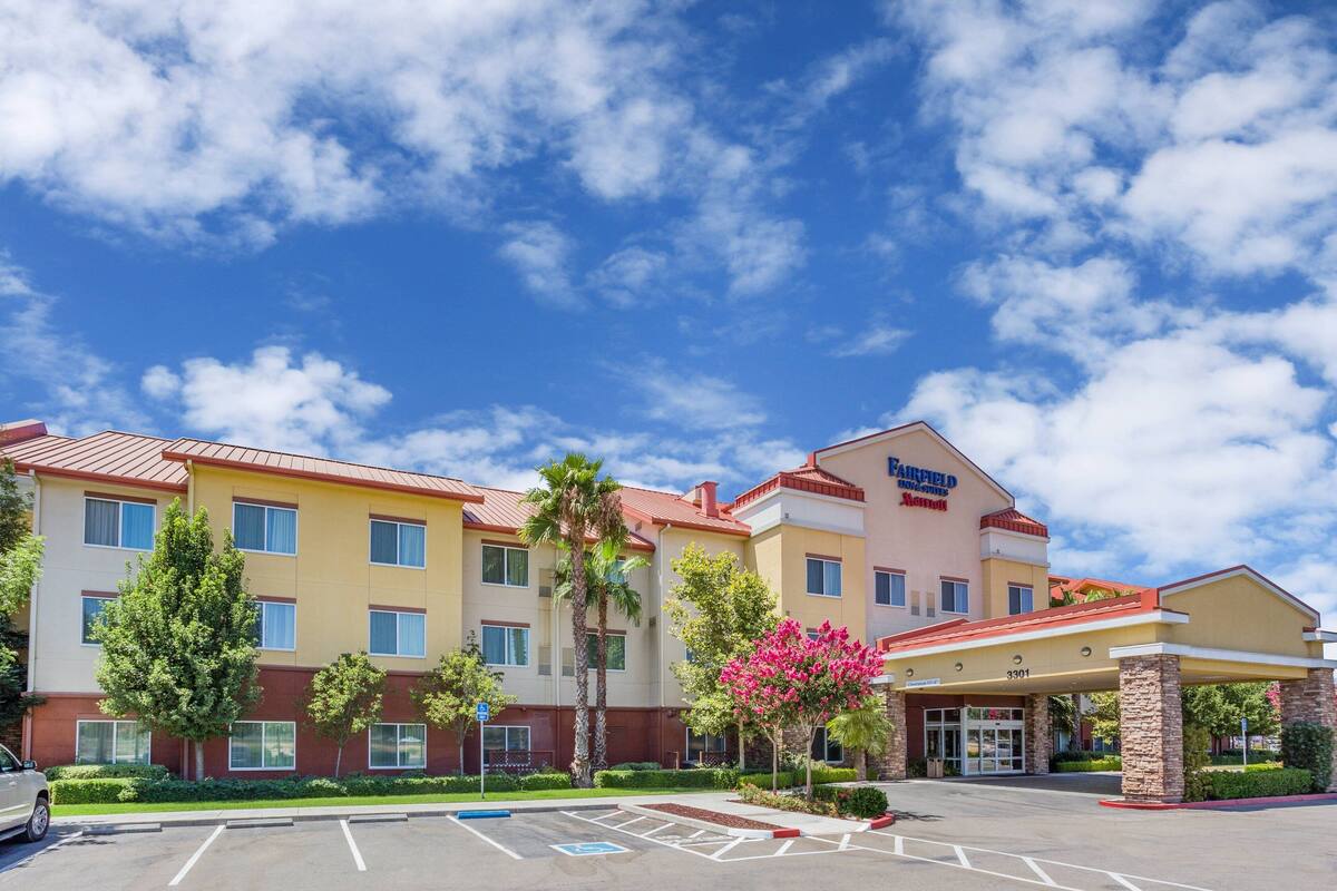 A Fairfield Inn & Suites hotel with a parking lot, palm trees, and a clear blue sky.