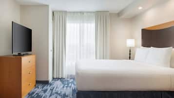 Quarto de hotel com uma cama, uma TV sobre uma cômoda de madeira e uma janela com cortinas.