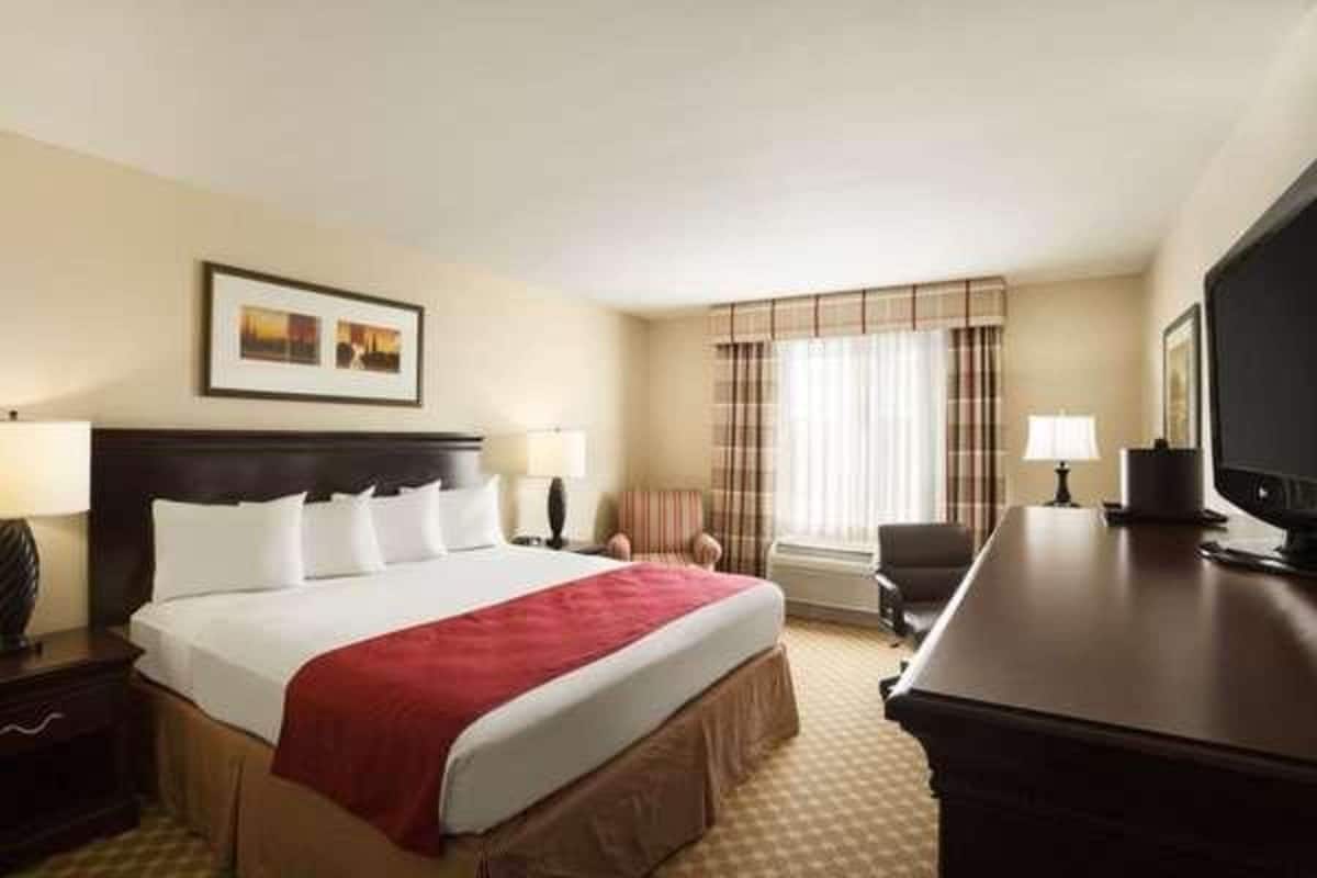 A hotel room with a large bed, a desk, a television, and a window with curtains.