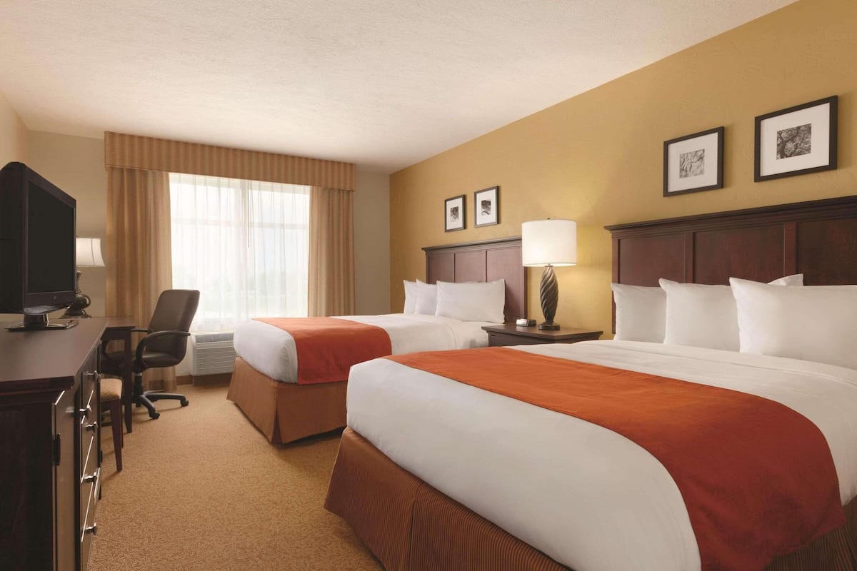 A hotel room with two beds, a desk with a computer, a chair, and a window with curtains.