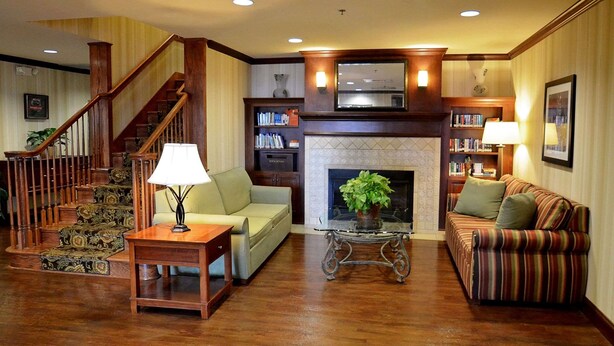 A spacious living room with a wooden staircase, a fireplace, a sofa, a coffee table, and a bookshelf. - Country Inn & Suites by Radisson, Knoxville at Cedar Bluff, TN (Knoxville)
