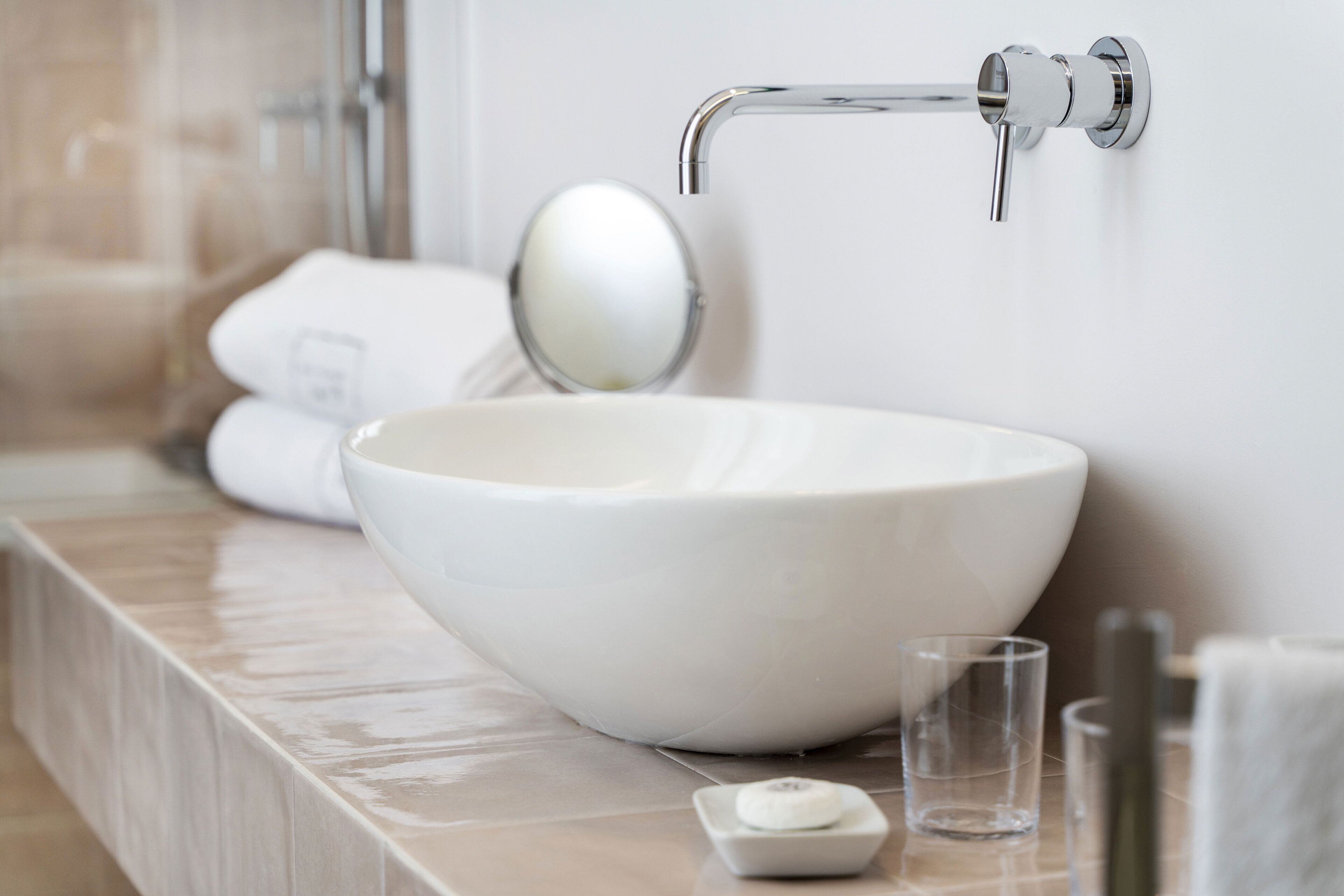 Un lavandino in ceramica bianca con un moderno rubinetto, un bicchiere d'acqua e un portasapone su un piano bagno.