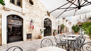 An outdoor café with stone walls, metal chairs, and tables under a white canopy. - Relais Antica Badia - San Maurizio 1619 (Ragusa)