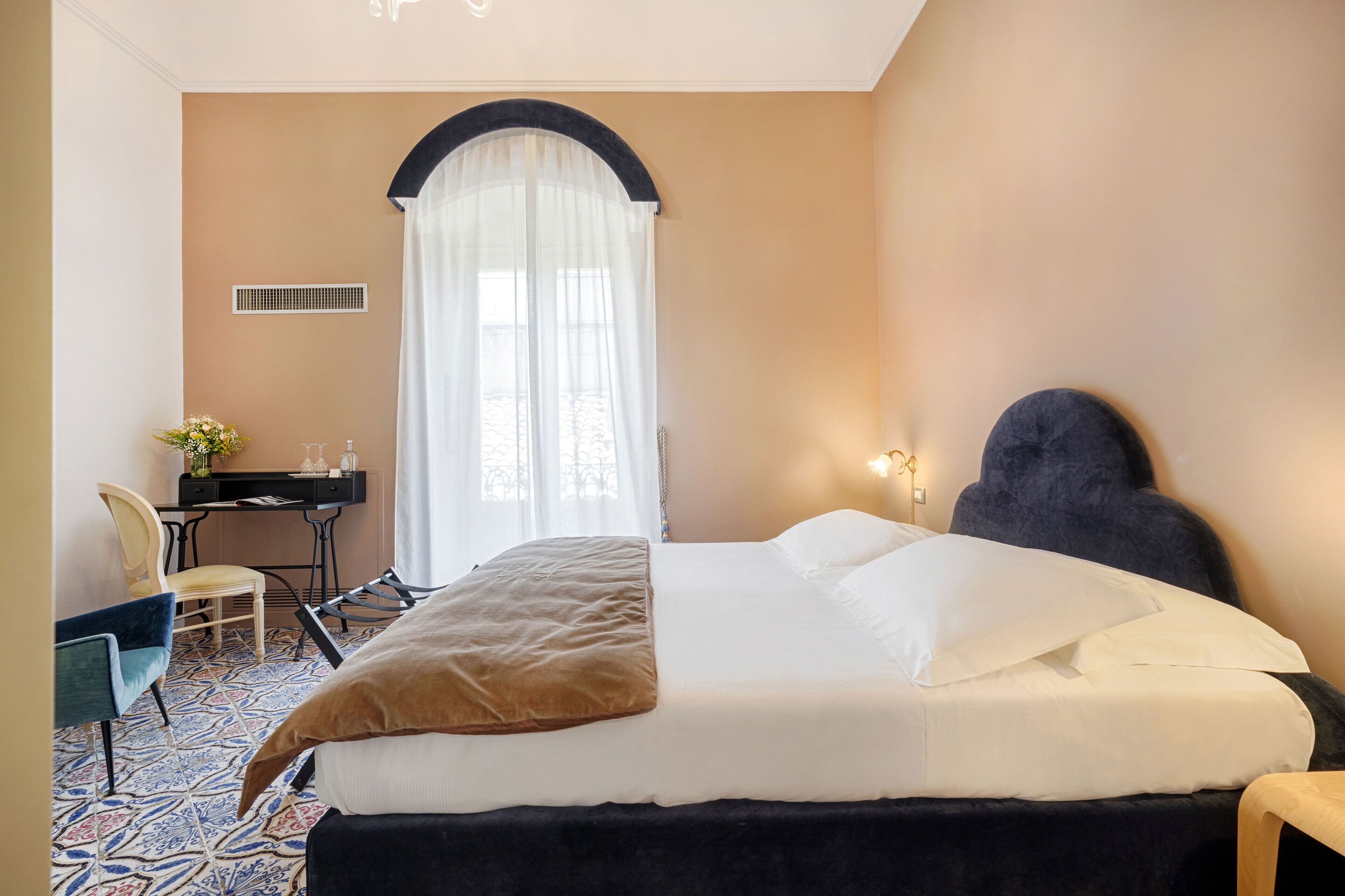 A hotel room with a bed, a desk, a chair, and a window with curtains.