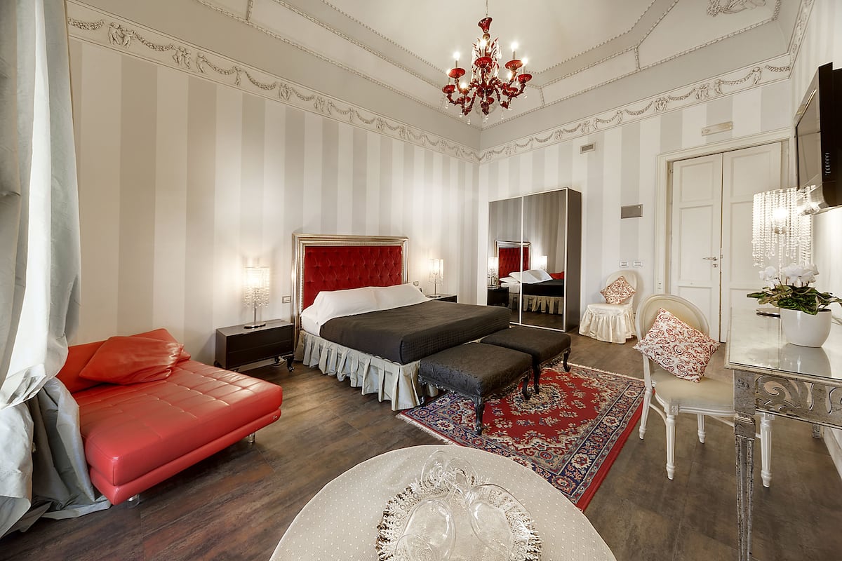 A hotel room with a large bed, a red sofa, a small table, and a mirror.