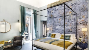 A modern bedroom with a four-poster bed, a chair, a round mirror, and a view of the city. - Relais Antica Badia - San Maurizio 1619 (Ragusa)