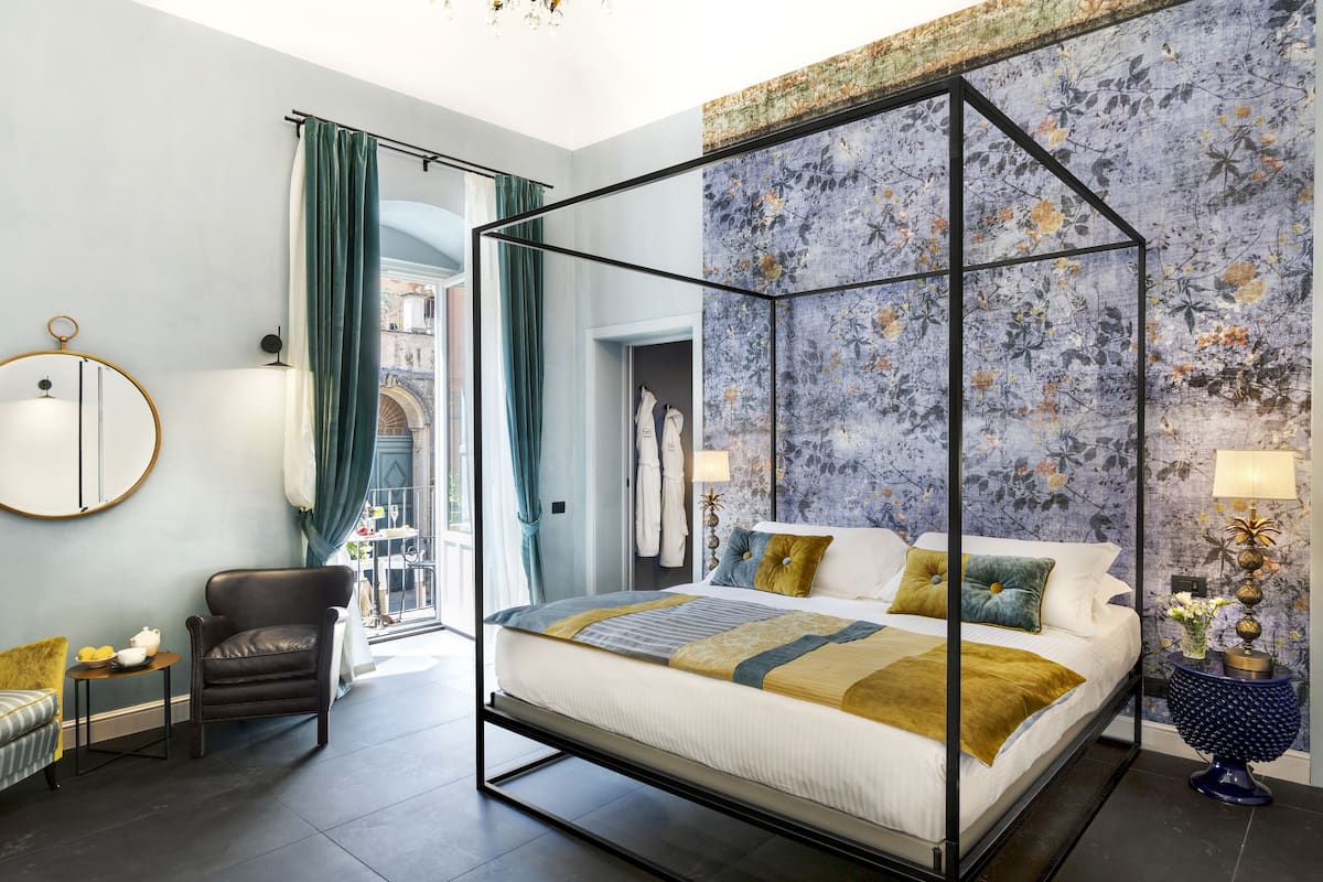 A modern bedroom with a four-poster bed, a chair, a round mirror, and a view of the city.