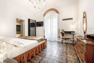 Une chambre d’hôtel comprenant un lit, un bureau, une chaise, une commode, une télévision et un lustre.