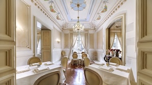 A formal dining room with ornate ceiling and chandeliers, multiple tables set for dining, and a marble floor. - Relais Antica Badia - San Maurizio 1619 (Ragusa)