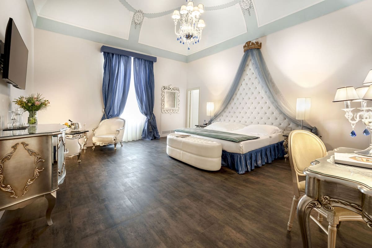 A bedroom with a large bed, a vanity with a mirror, a desk, and a chandelier.