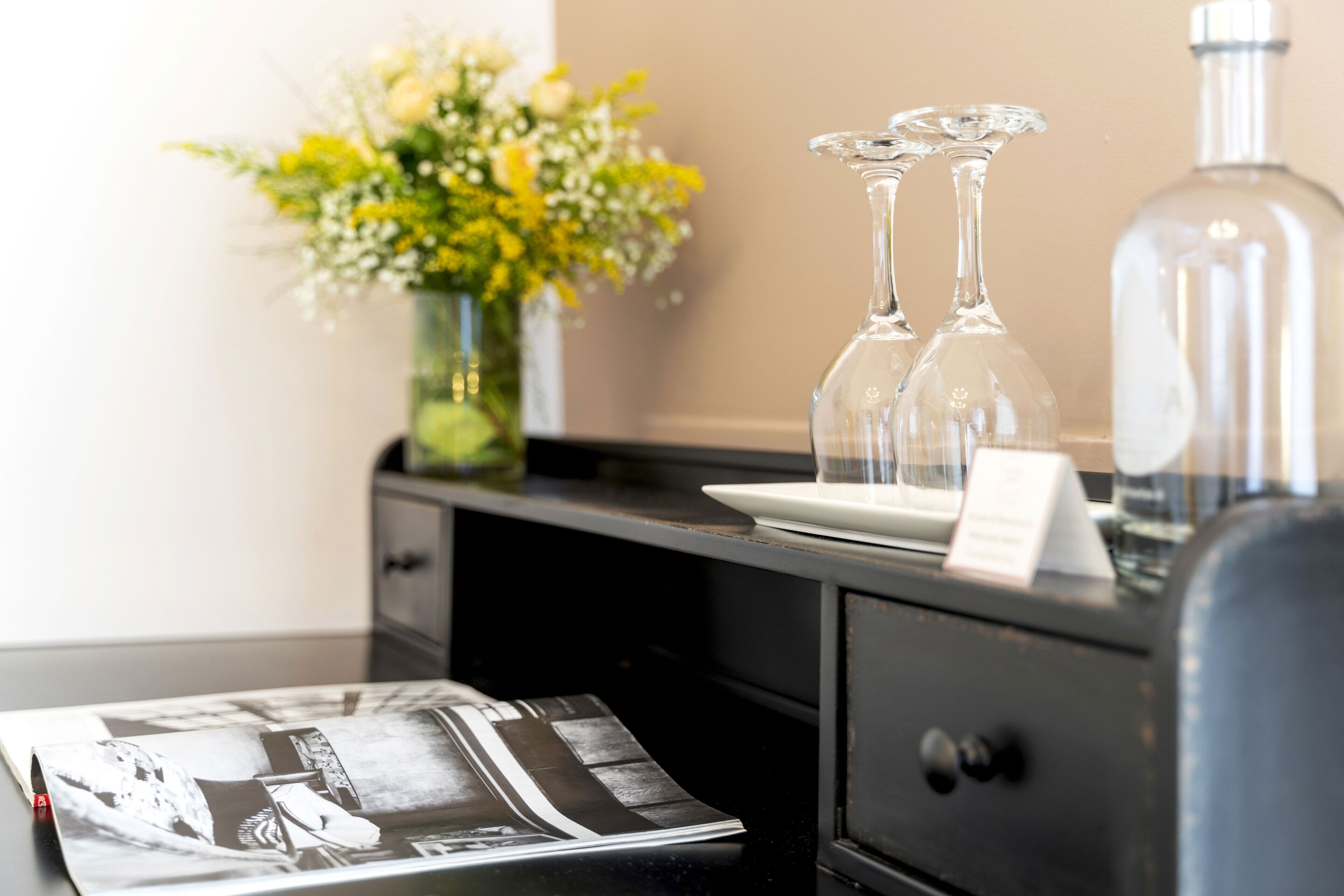 A hotel reception area with a black desk, a vase of flowers, two clear glass bottles, and a bottle of water.