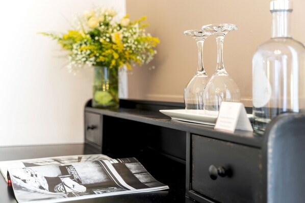Un espace d’accueil d’hôtel avec un comptoir noir, un vase de fleurs, deux bouteilles en verre transparent et une bouteille d’eau.