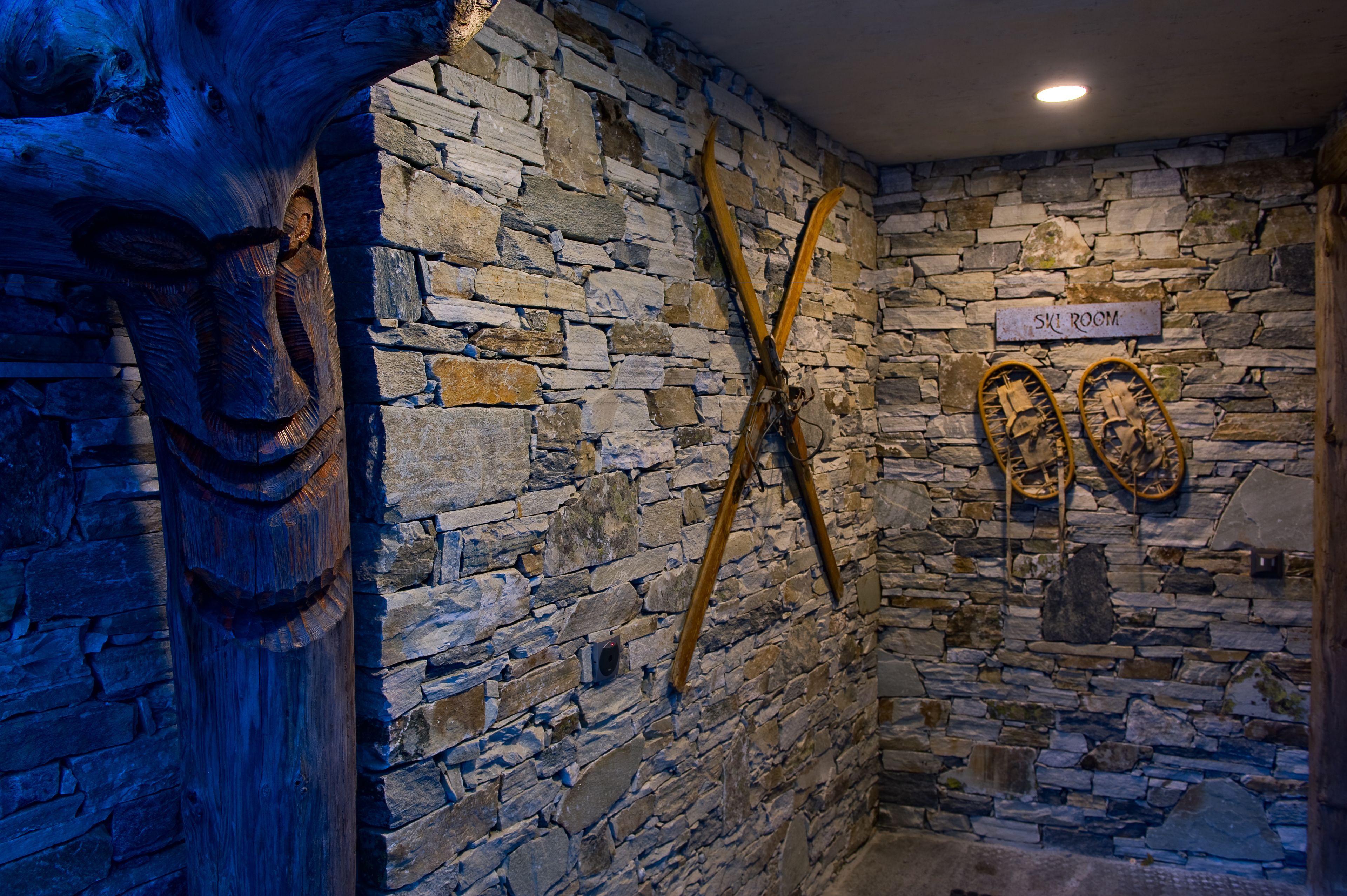 Un mur de pierre orné d’une sculpture en bois et sur lequel sont fixés des paires de skis.
