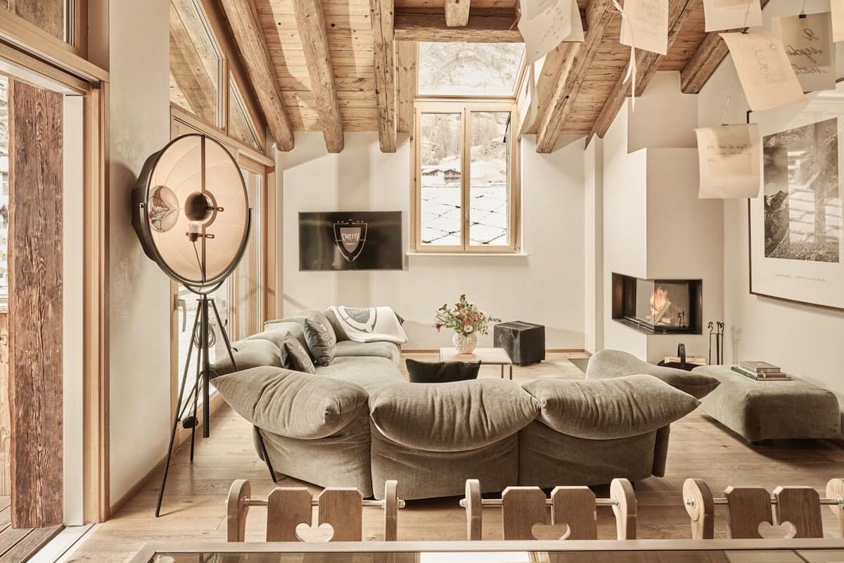 Un salon chaleureux avec un canapé d’angle, une cheminée et une grande fenêtre.