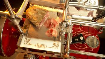 Un cortador de fiambres Berkel rojo con un trozo grande de carne y jamón en lonchas finas.