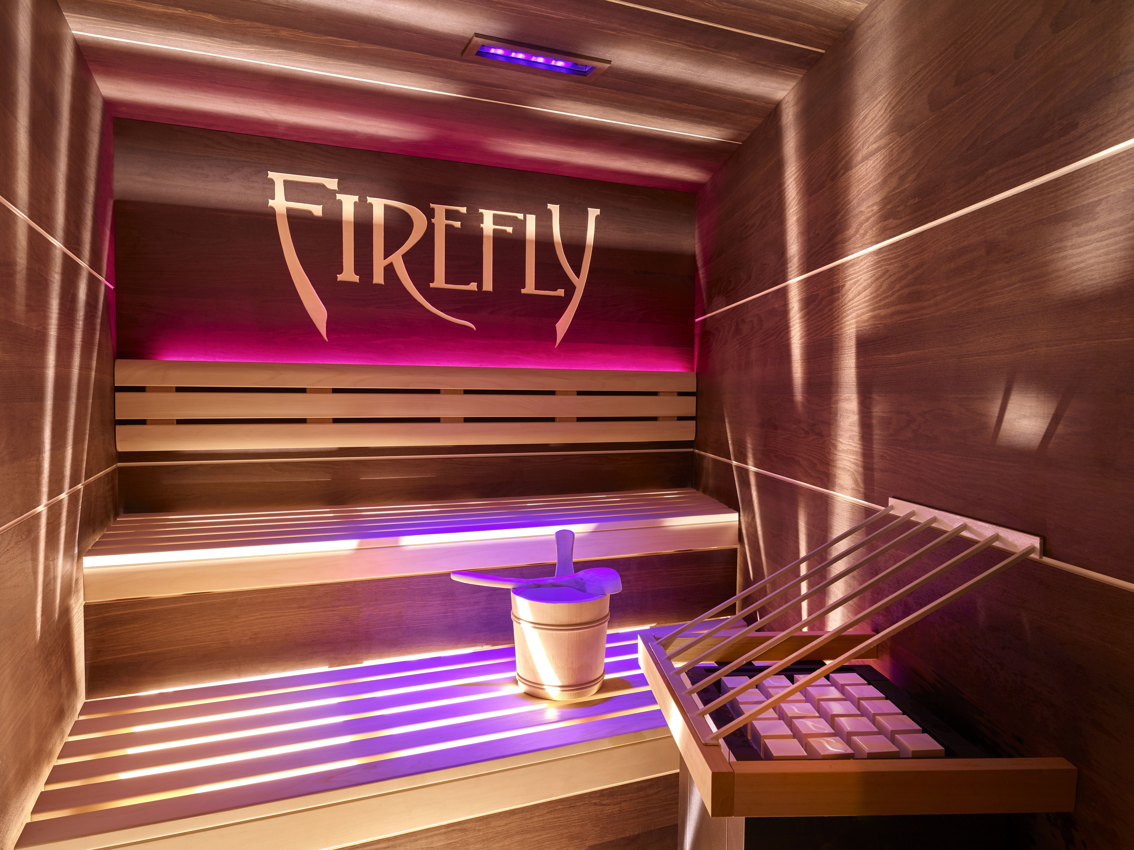 A sauna with a sign reading "Firefly," wooden benches, and a small table with a drink container.