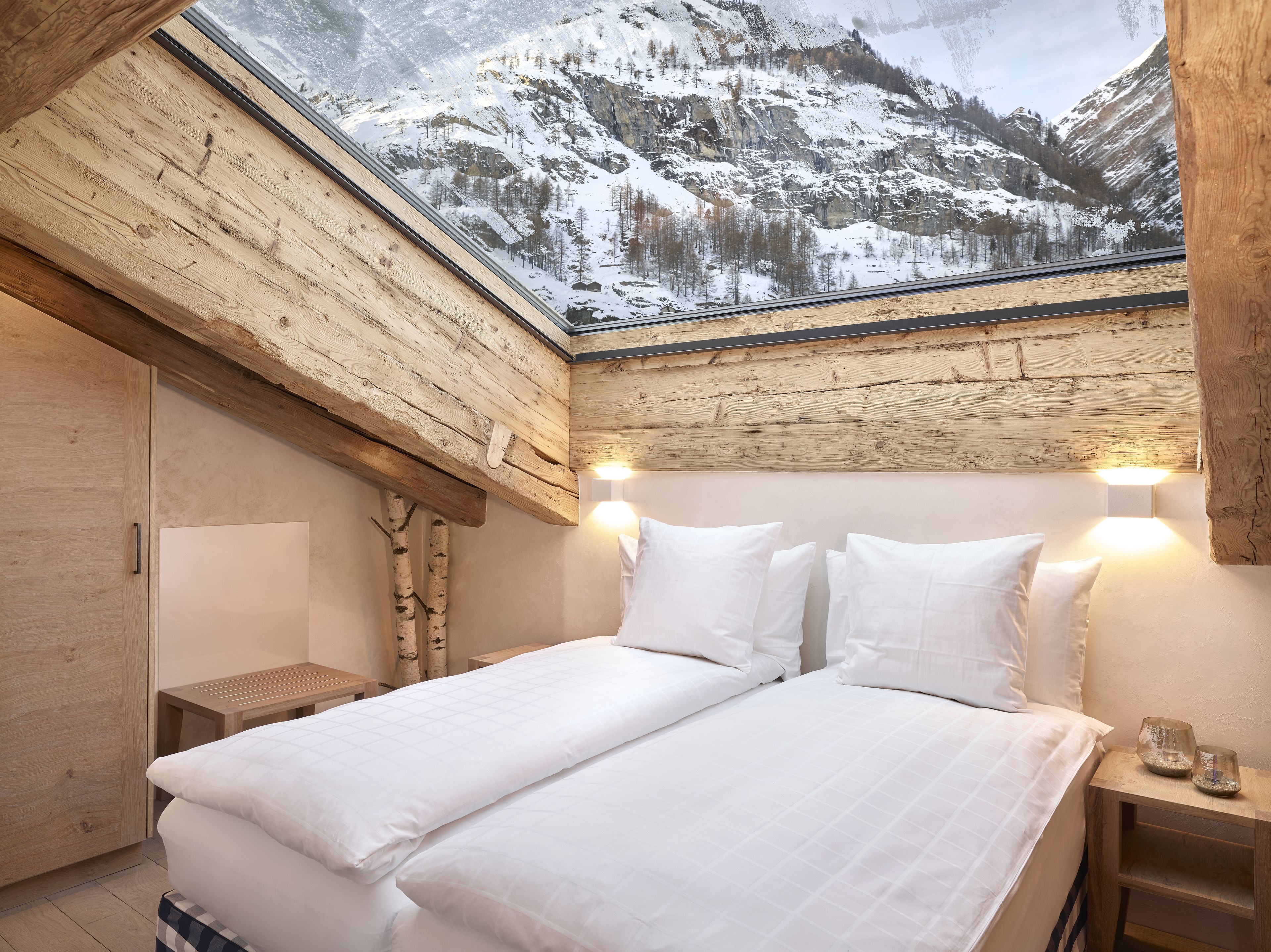 Ein Schlafzimmer mit einem großen Bett, einem Holzkopfende und einem Dachfenster mit Blick auf einen verschneiten Berg.