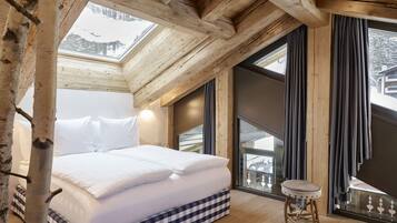 A bedroom with a large bed, a small stool, and a view of a snowy mountain through a window.