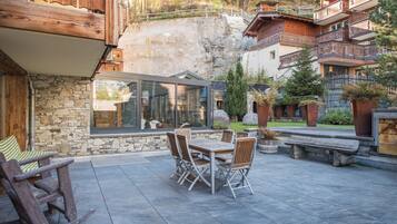 A patio with a stone wall, wooden furniture, and a view of a mountainous area.