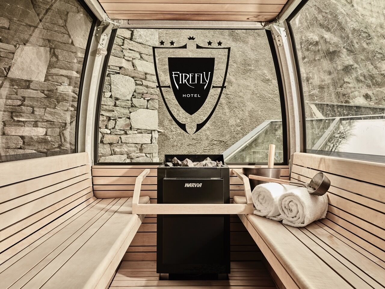 A cozy, stone-walled room with a Harvia grill, a bench, and neatly rolled towels.