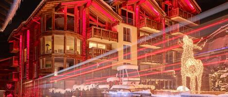 A multi-story building with balconies and large windows, featuring a snow-covered ground and a decorative snow sculpture.