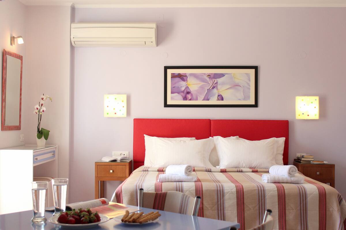Ein Hotelzimmer mit Bett, Nachttischen, Schreibtisch mit Stuhl, Spiegel und einer Wand-Klimaanlage.