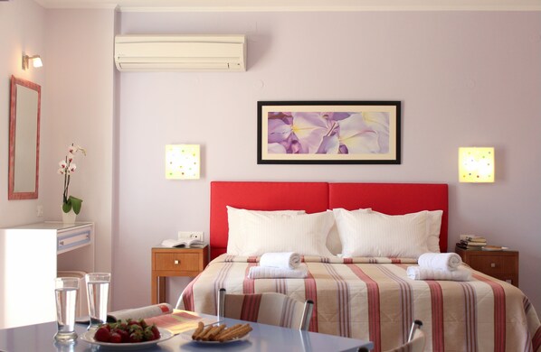 A hotel room with a bed, bedside tables, a desk with a chair, a mirror, and a wall-mounted air conditioner. - Amaryllis Hotel Apartments (Nafplio)