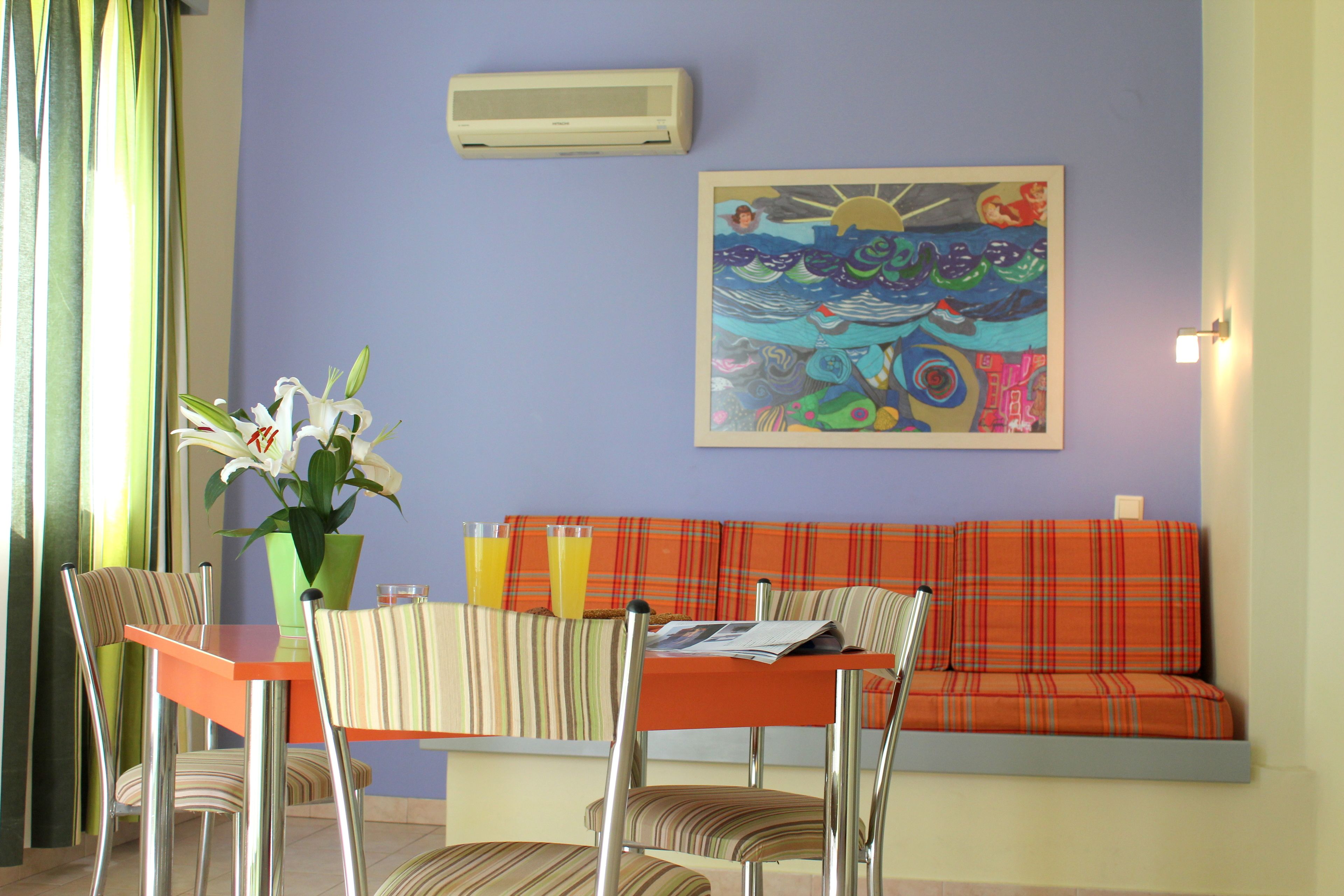 A dining area with a table, chairs, a vase with flowers, and a colorful painting on the wall.