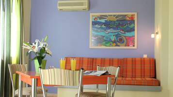 A dining area with a table, chairs, a vase with flowers, and a colorful painting on the wall.
