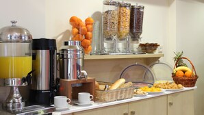 A breakfast buffet with coffee machines, orange juice, cereal, and a fruit basket. - Amaryllis Hotel Apartments (Nafplio)