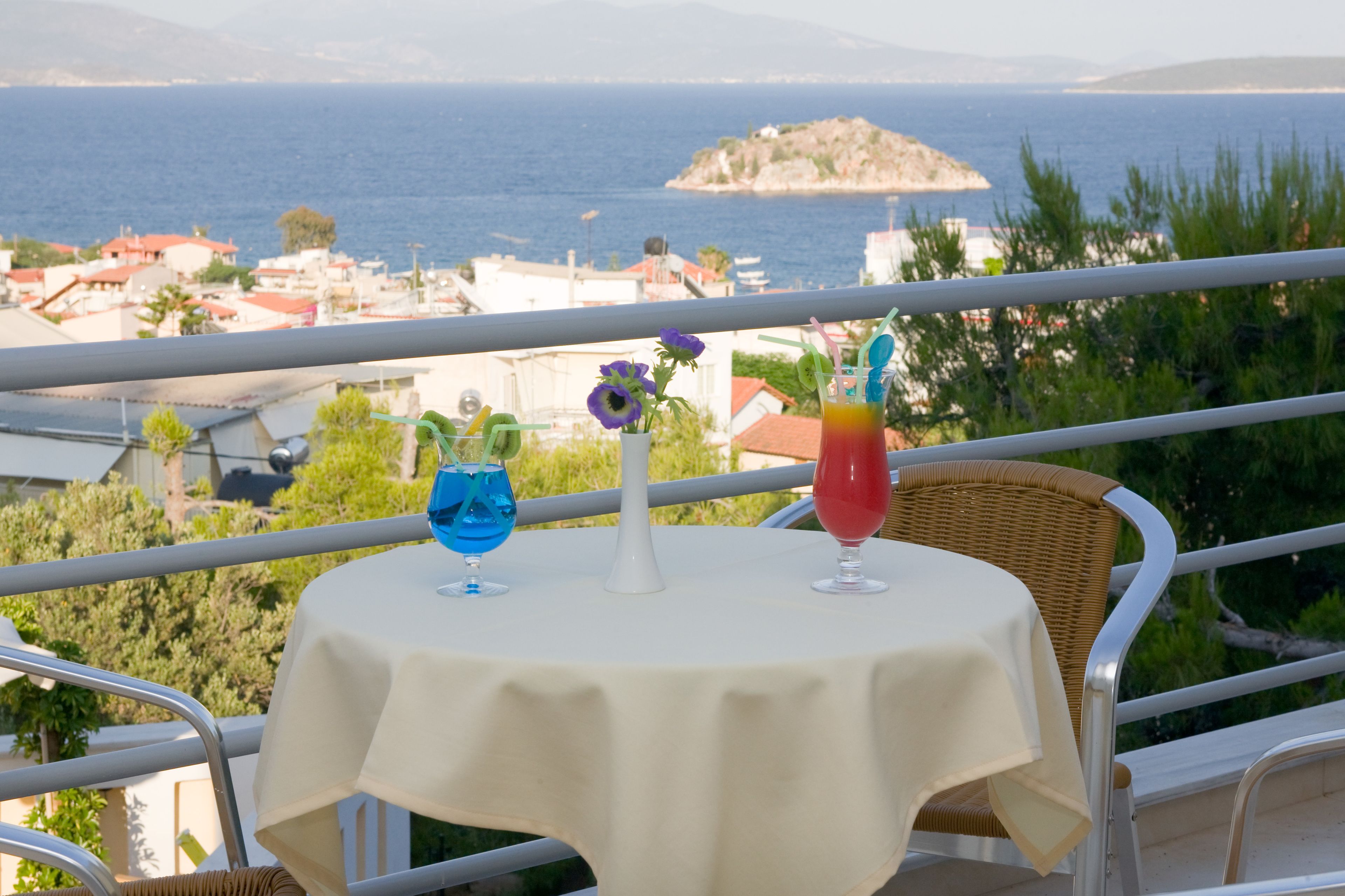 Ein Balkon mit Tisch für zwei Personen, mit Blick auf die Küste, Häuser und eine kleine Insel.