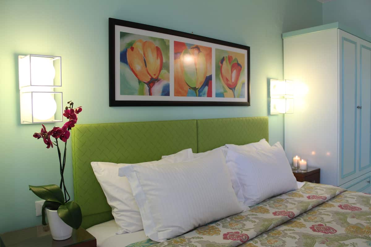 Ein Hotelzimmer mit einem grünen Kopfteil, weißer Bettwäsche, einem gerahmten Blumenbild über dem Bett und Nachttischlampen.