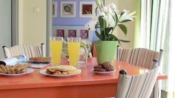 Una mesa de comedor con sillas a rayas, platos de comida, vasos de zumo de naranja y un jarrón con flores blancas.