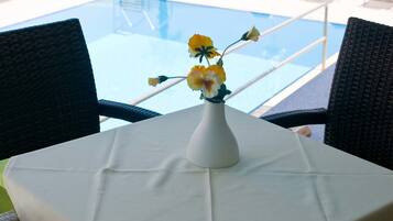 A table with a white tablecloth, a vase with yellow flowers, and a view of a pool and lounge chairs.