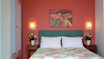 A bedroom with a teal headboard, two white pillows, a floral bedspread, a painting on the wall, and two bedside lamps.