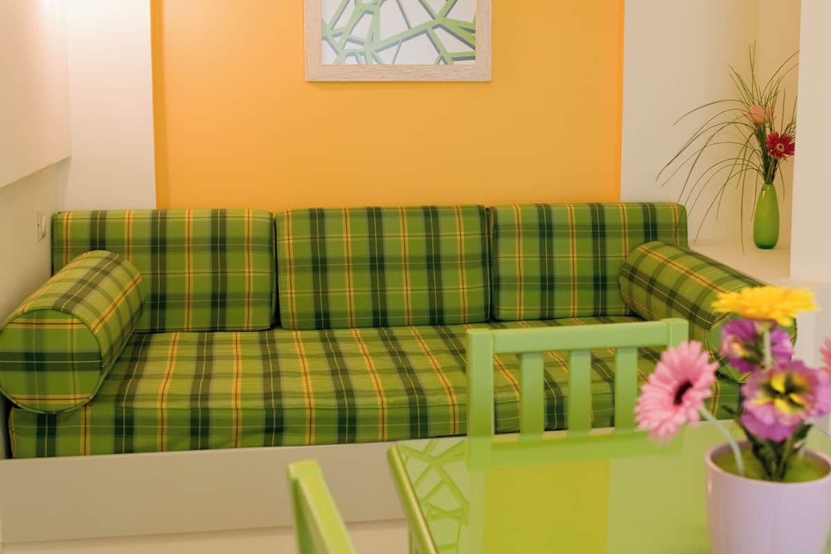 Ein grünes Karo-Sofa an einer gelben Wand, ein grüner Sessel und eine Vase mit Blumen.